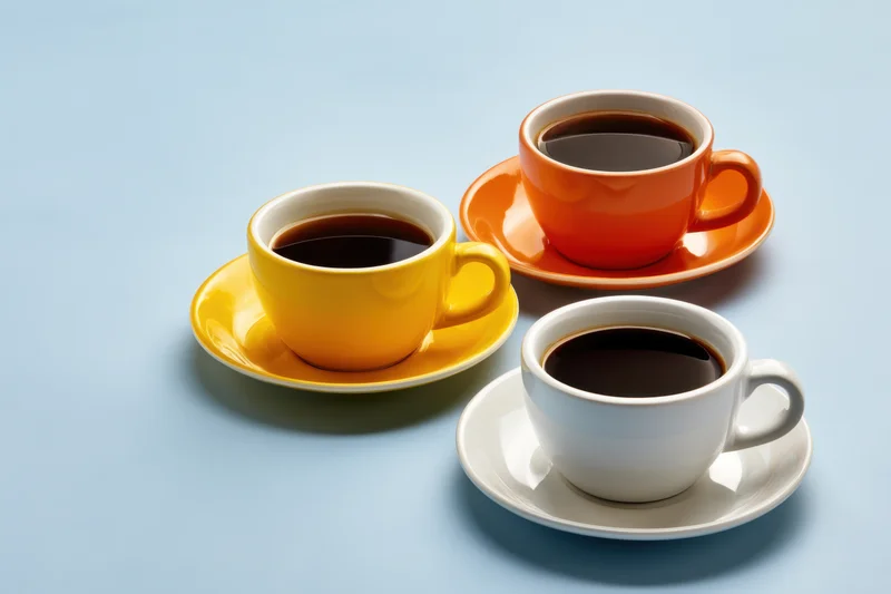 Three colorful coffee cups with saucers arranged on a light blue surface