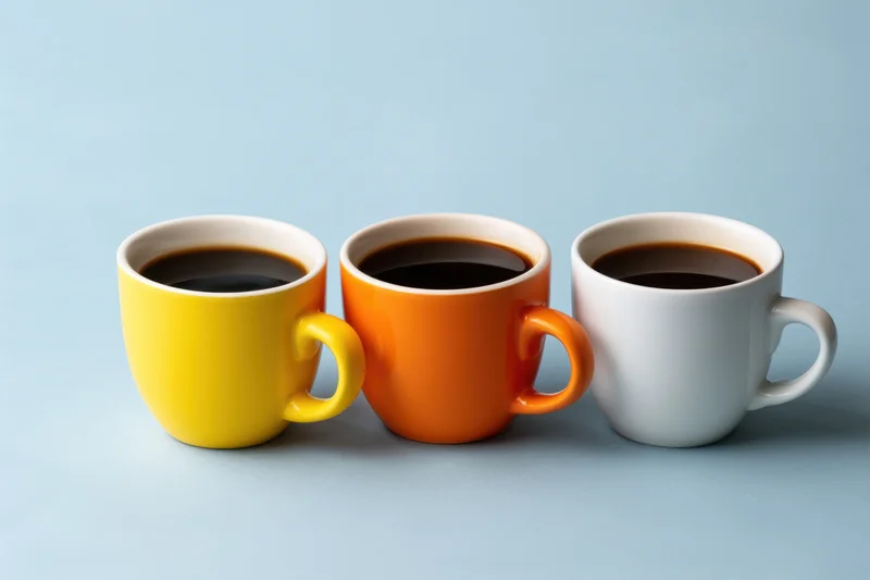 Three colorful coffee mugs filled with black coffee arranged in a row on a light blue surface
