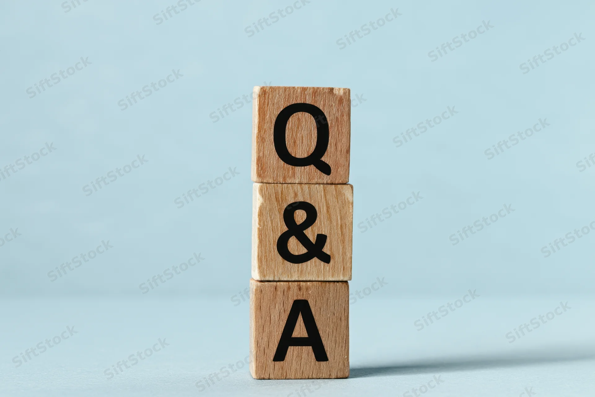 Three wooden blocks stacked vertically with letters q, ampersand, and a forming a question and answer symbol on a light blue surface