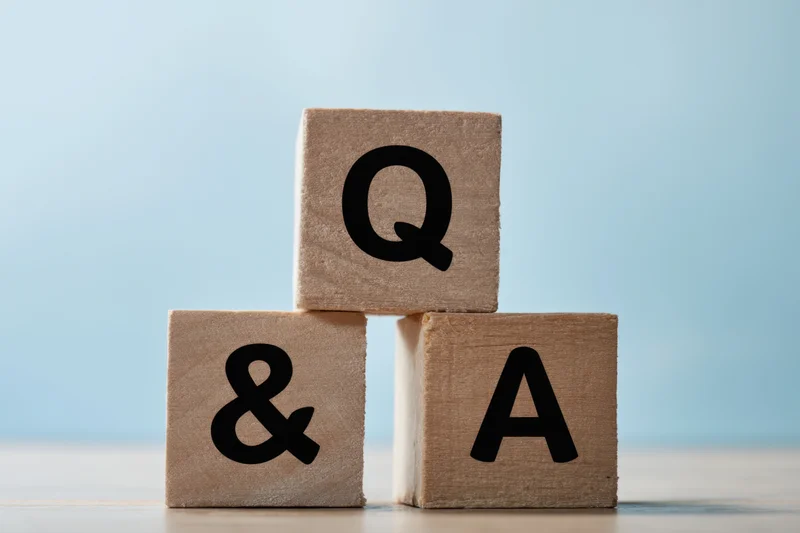Three wooden blocks stacked in pyramid shape with letters q, a, and ampersand on them against a light blue background