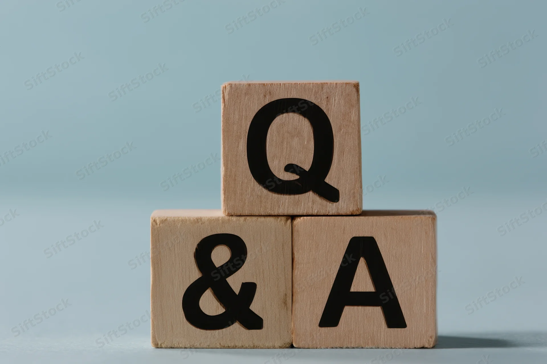 Three wooden blocks stacked with letters q, ampersand, and a forming a question and answer symbol on a light blue surface
