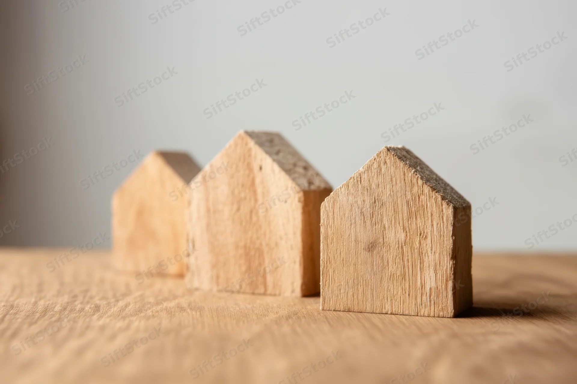 Three wooden house models of varying sizes arranged in a row on a wooden surface