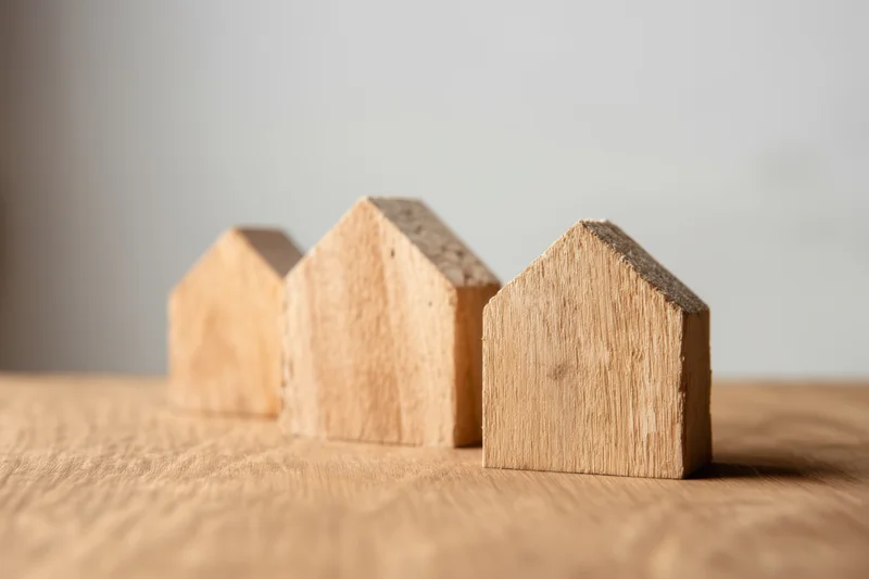Three wooden house models of varying sizes arranged in a row on a wooden surface