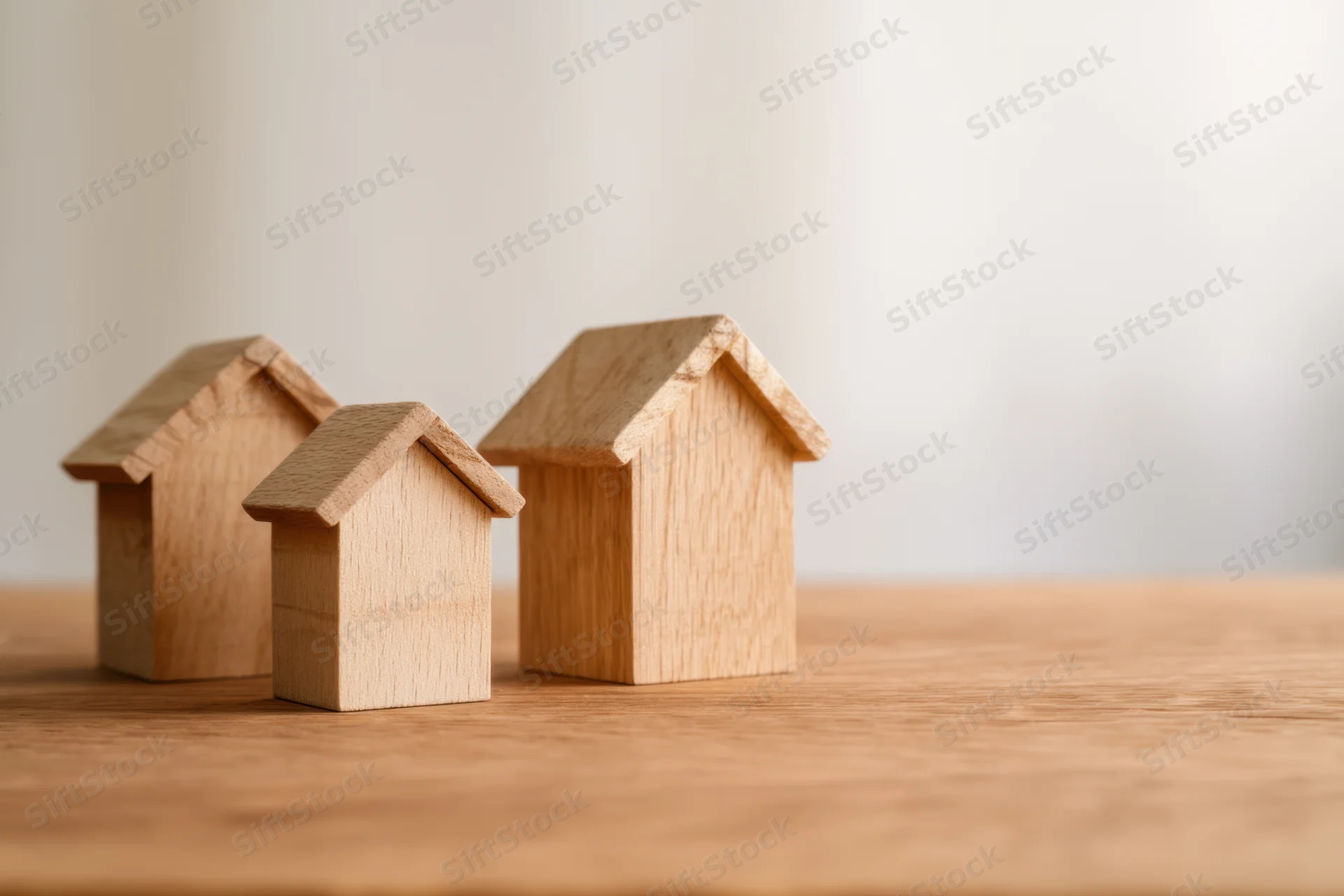 Three wooden house models of varying sizes arranged on a wooden surface