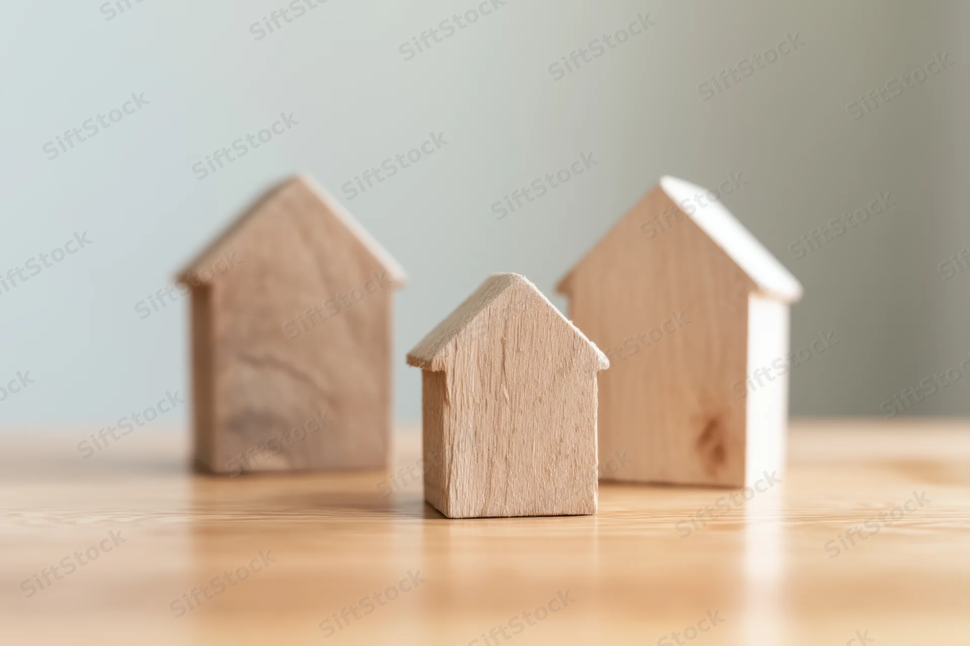 Three wooden house models of varying sizes arranged on a wooden surface with shallow depth of field