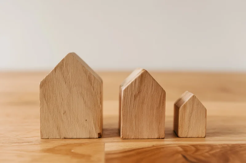 Three wooden house models of varying sizes arranged in a row on a wooden surface