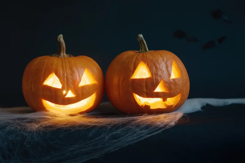 Two carved pumpkins glowing warmly on a cobweb-covered surface at night