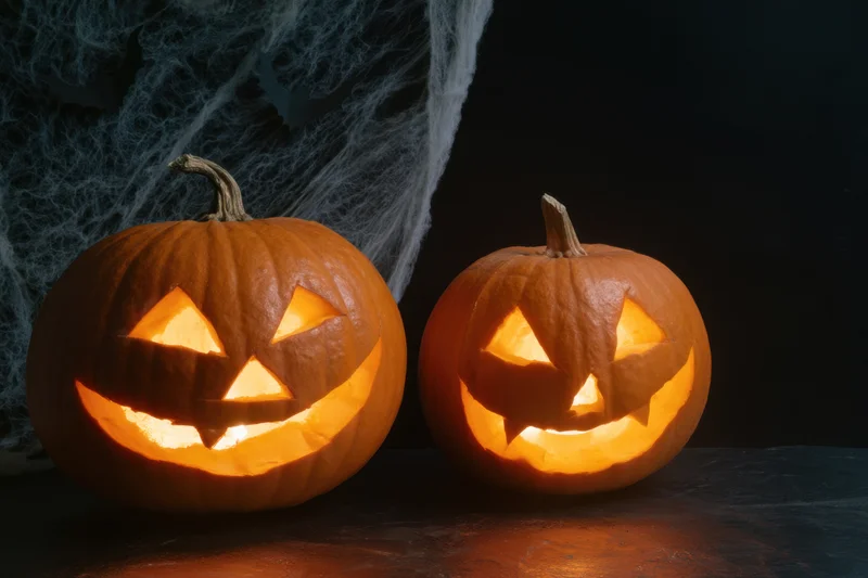 Two carved pumpkins glowing warmly on a dark surface with spiderweb backdrop