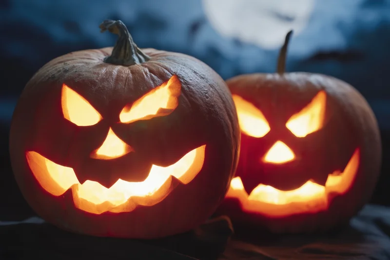 Two carved pumpkins with glowing menacing faces at night under moonlight