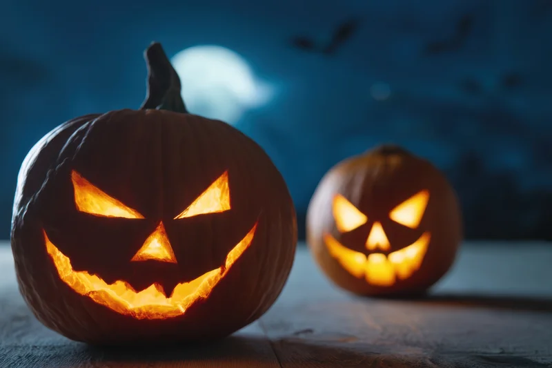 Two carved jack-o-lanterns with menacing expressions glowing on a wooden table at night under a full moon