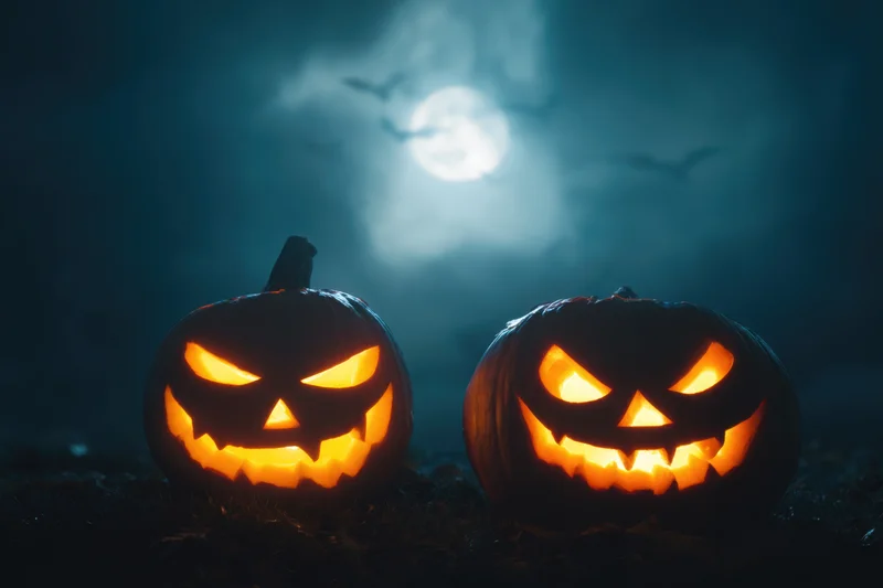 Two carved jack-o-lanterns with menacing expressions glowing in the dark under a full moon