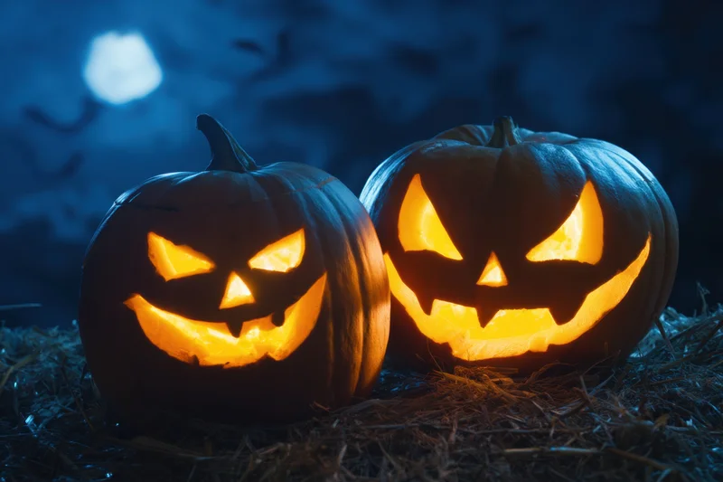 Two carved jack-o-lanterns with menacing expressions glowing on hay at night under moonlight
