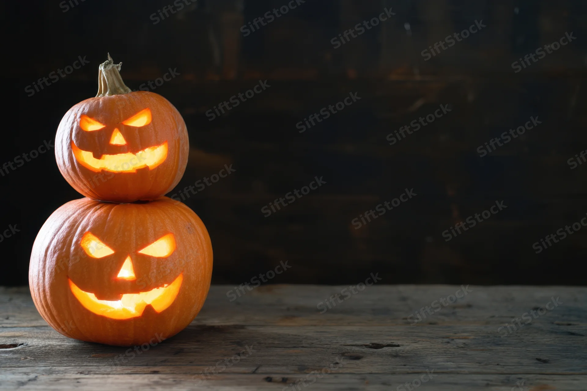Two carved pumpkins stacked with glowing faces on a wooden table in a dark room