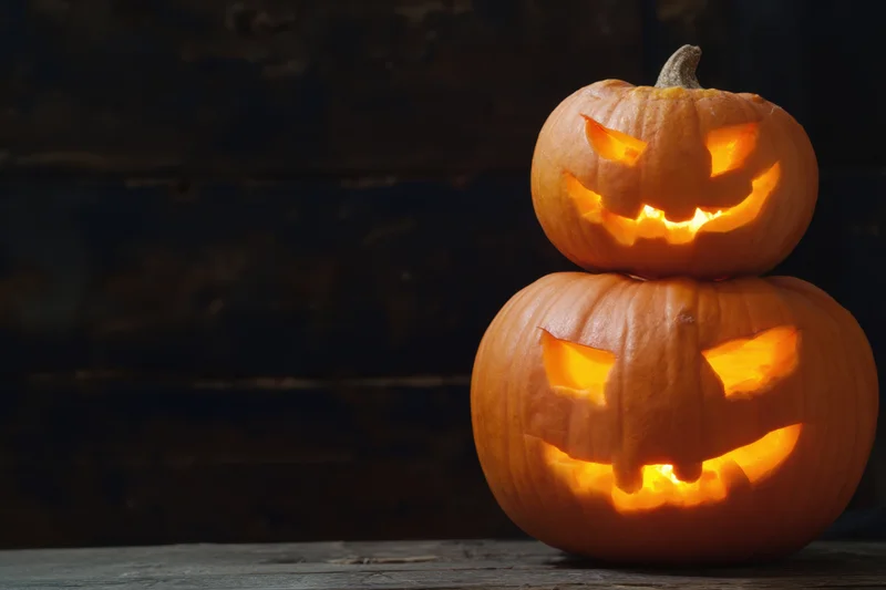 Two carved pumpkins stacked on a wooden table glowing with candlelight against a dark background
