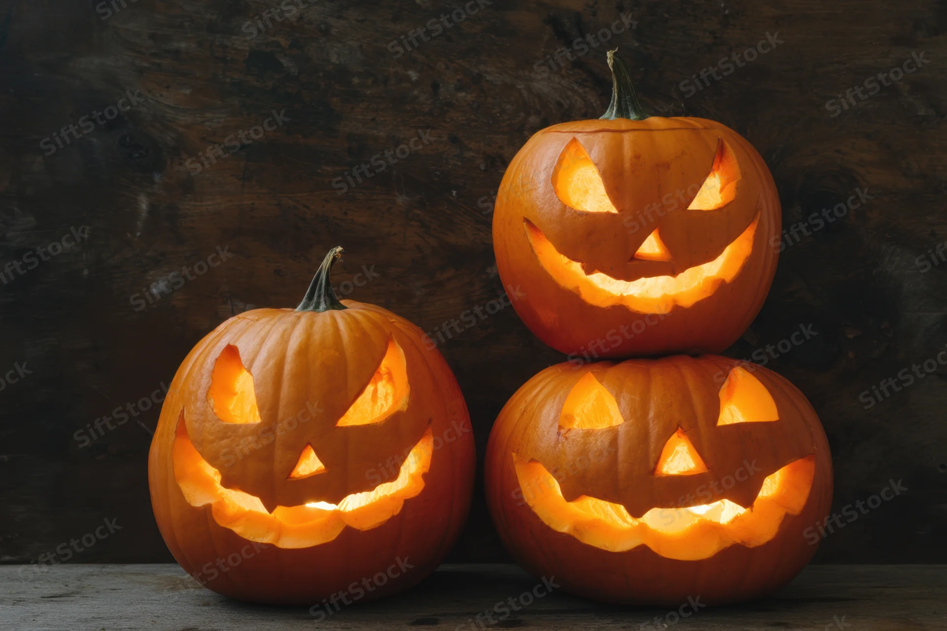 Three carved pumpkins arranged with one stacked on top, glowing from within on a wooden surface