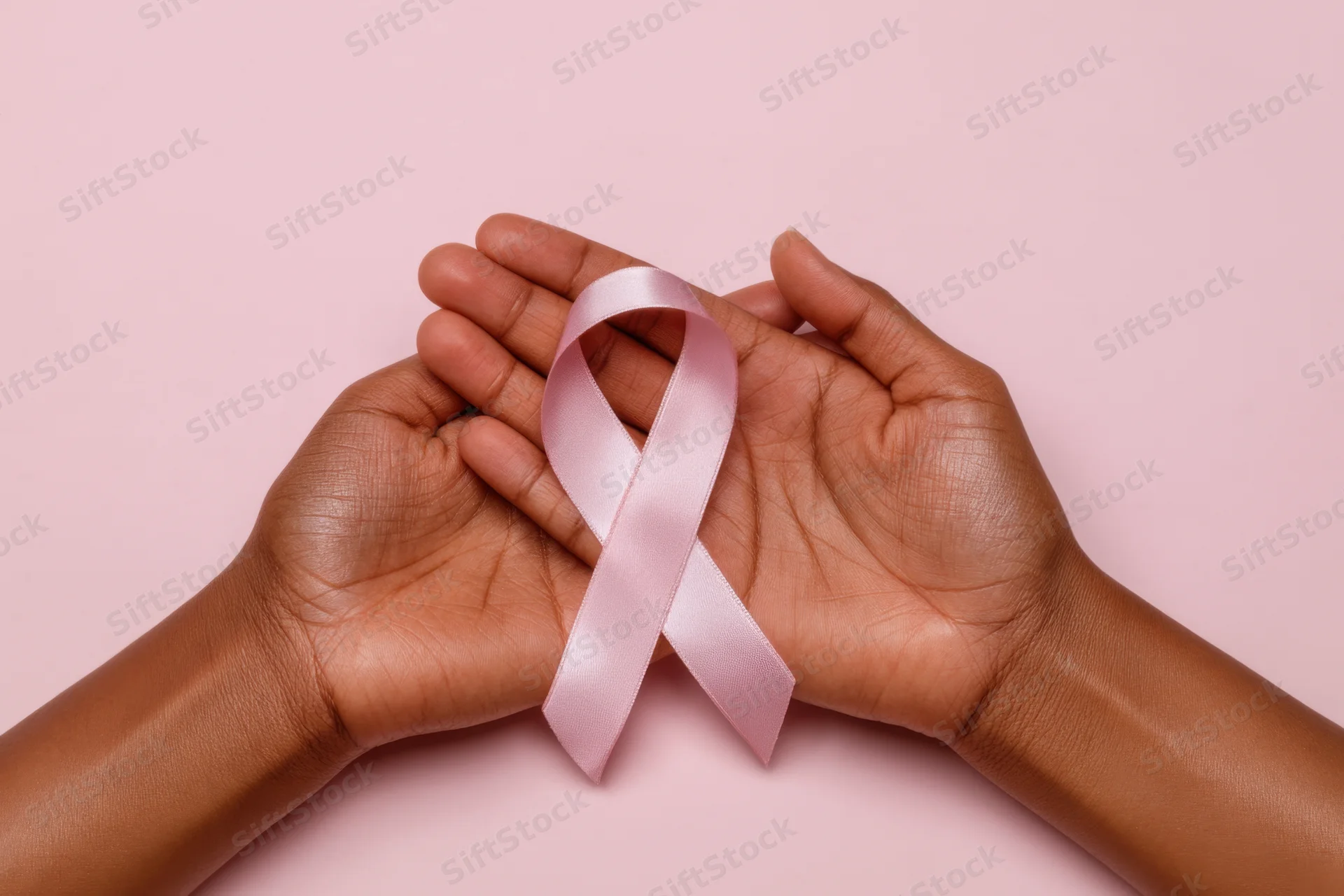 Two hands holding a pink awareness ribbon against a pink background
