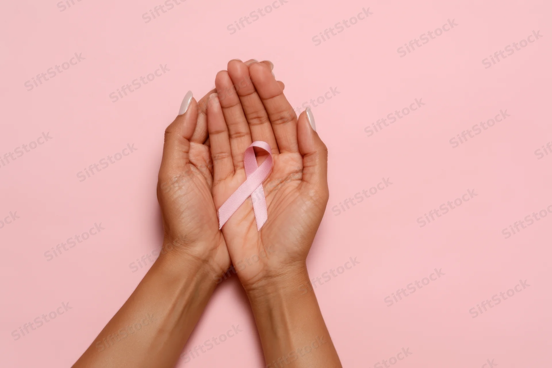 Two hands gently holding a pink awareness ribbon against a solid pink background