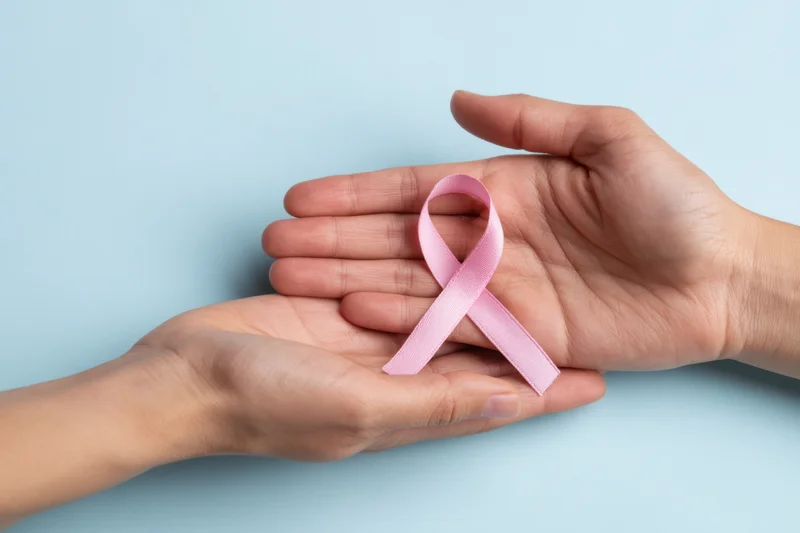 Two hands gently holding a pink ribbon against a soft blue background