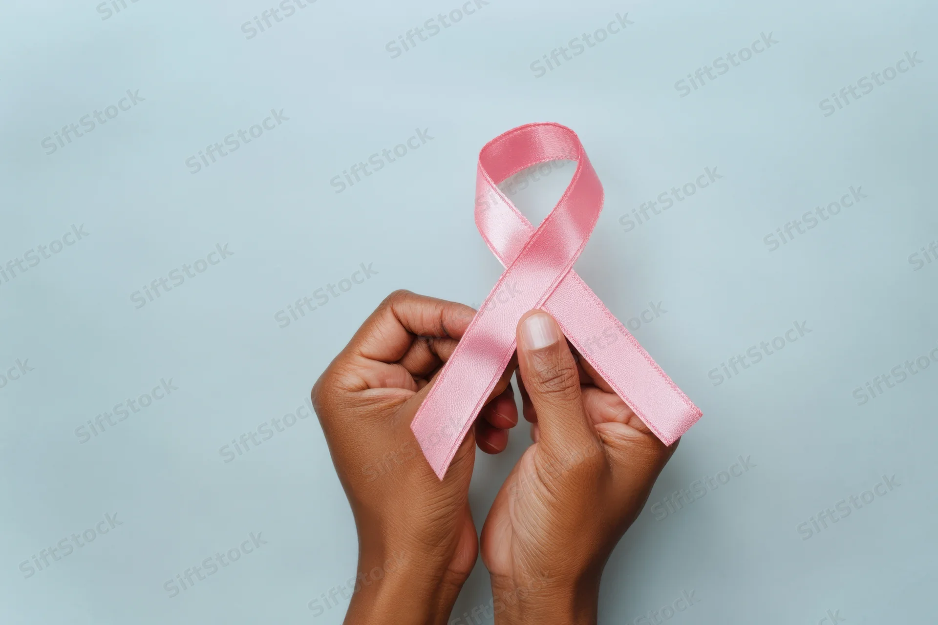 Two hands holding a pink ribbon against a soft blue background