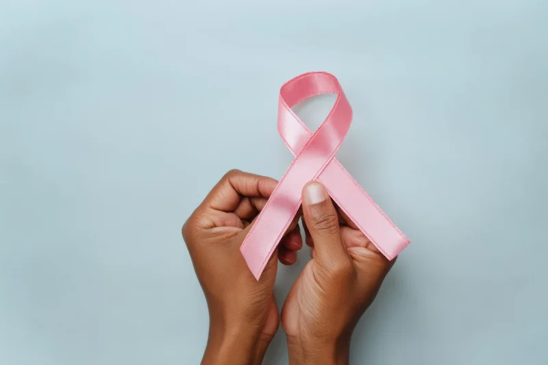 Two hands holding a pink ribbon against a soft blue background