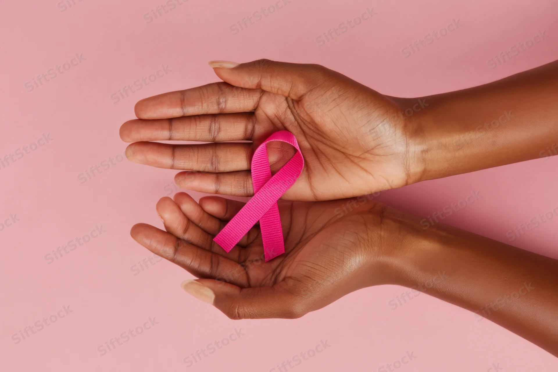 Two hands gently holding a pink ribbon against a soft pink background