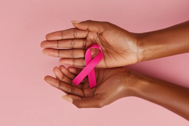 Two hands gently holding a pink ribbon against a soft pink background