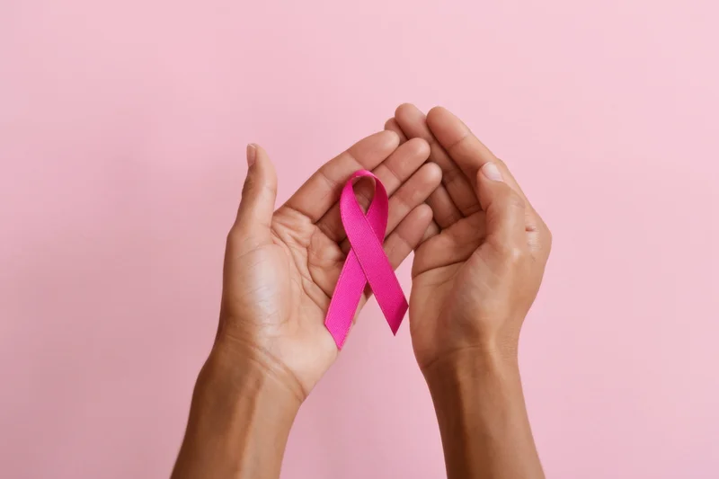 Hands gently holding a pink ribbon against a pink background