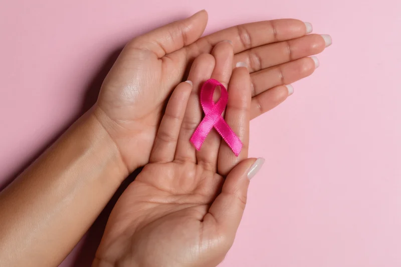 Two hands gently holding a pink ribbon against a soft pink background
