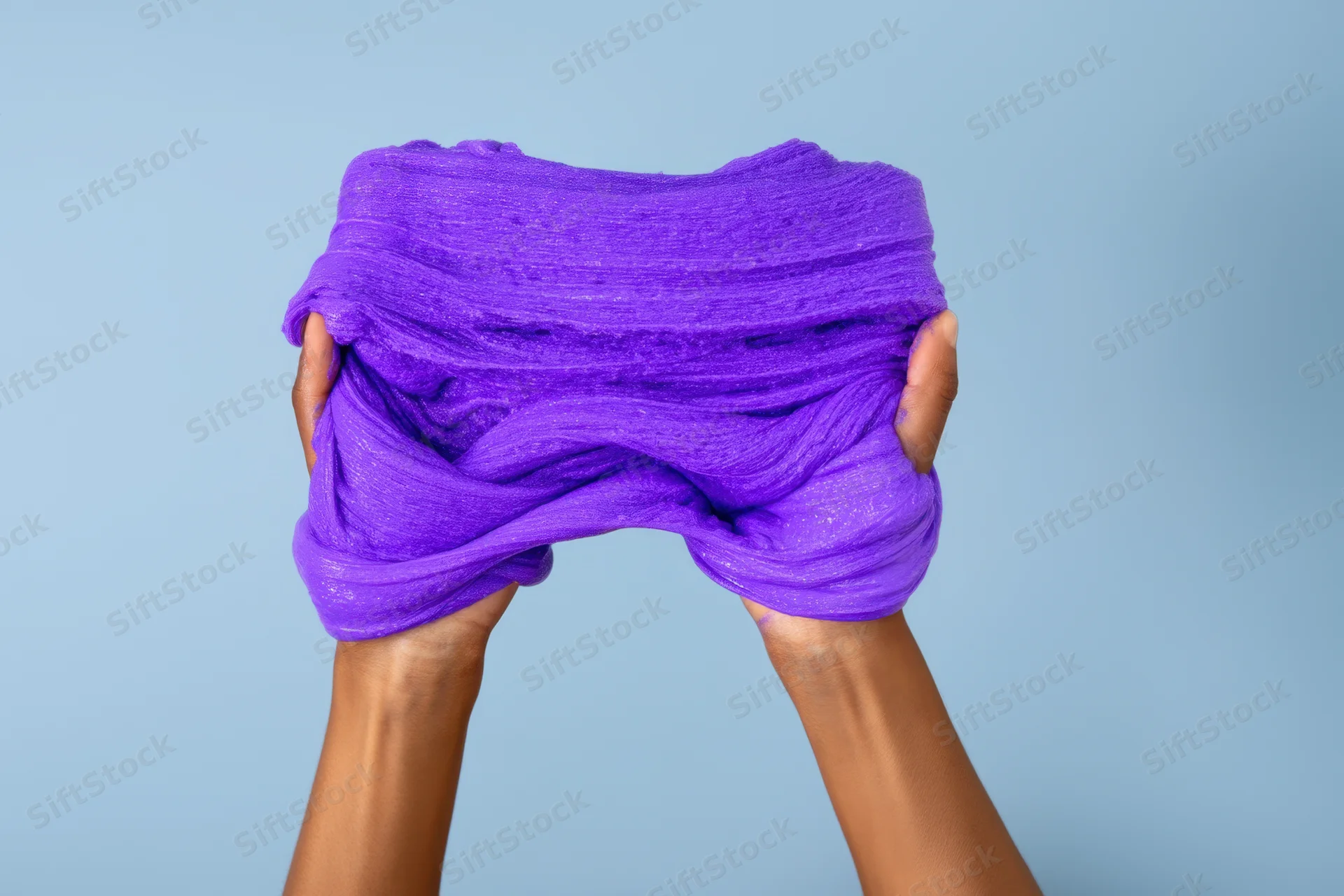 Hands stretching vibrant purple slime against a soft blue background
