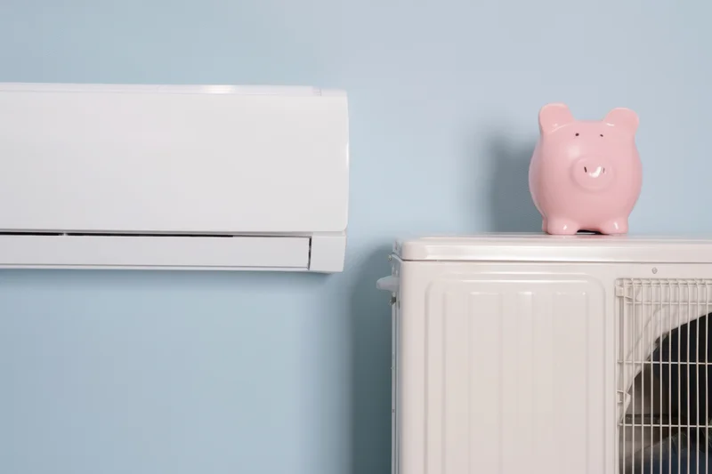 White air conditioning unit mounted on blue wall beside white appliance with pink piggy bank on top