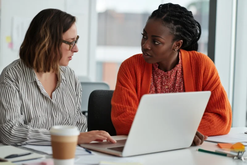 Two women collaborating on a laptop in an office meeting setting