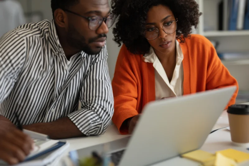 Two professionals collaborating on a laptop in an office workspace