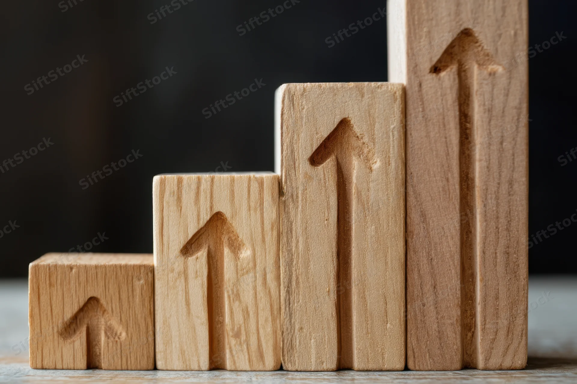 Wooden blocks arranged in ascending stair-step formation each with carved upward arrow on front face on textured surface