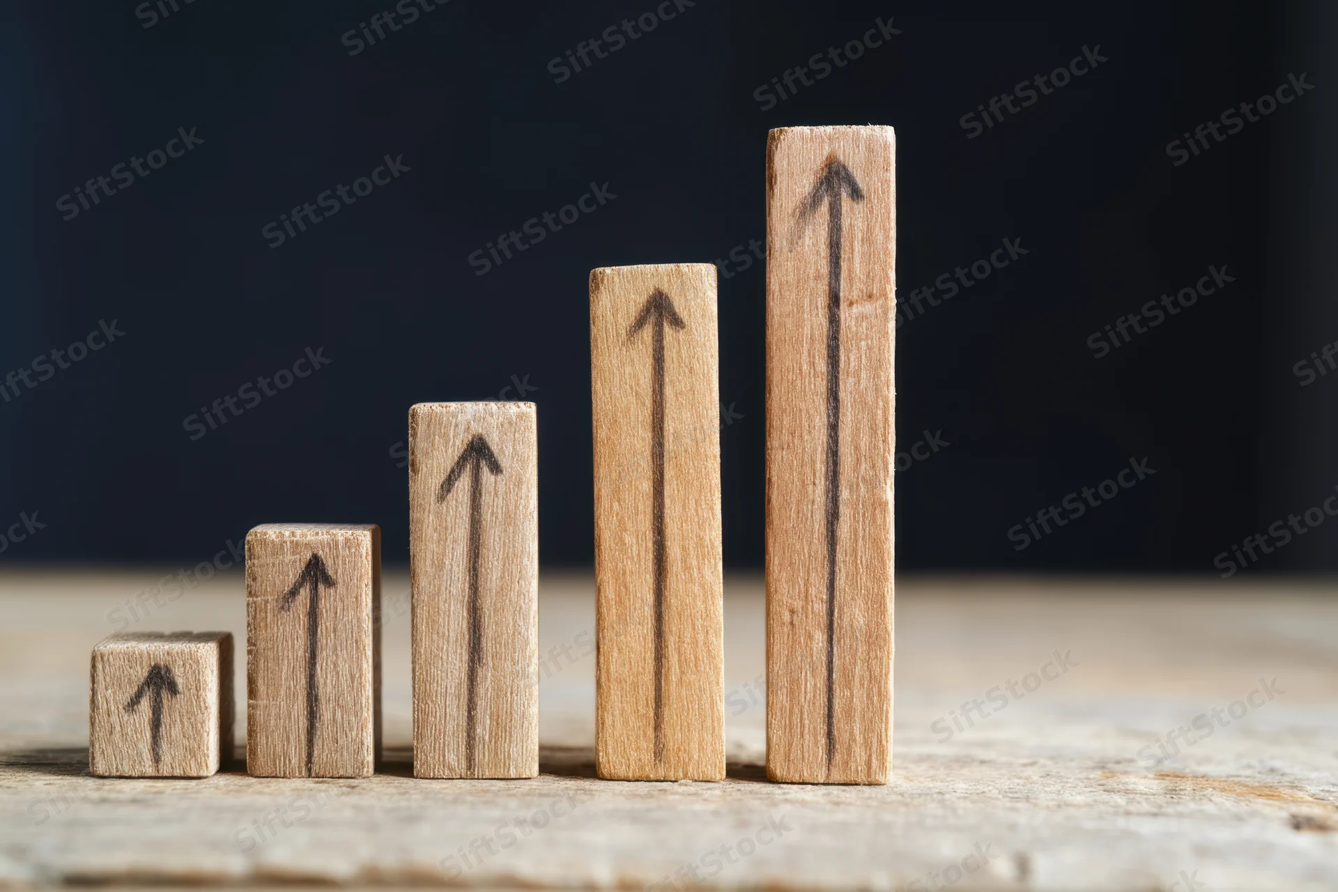 Wooden blocks with upward arrows arranged in ascending height on a rustic table surface