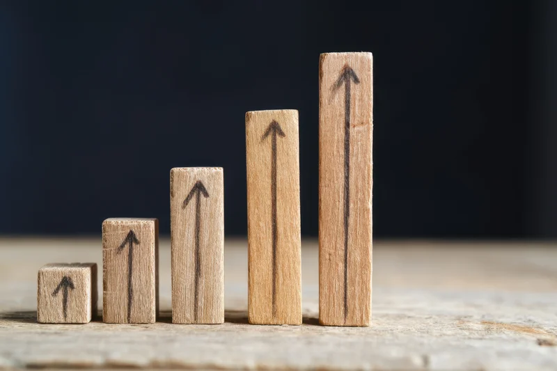Wooden blocks with upward arrows arranged in ascending height on a rustic table surface