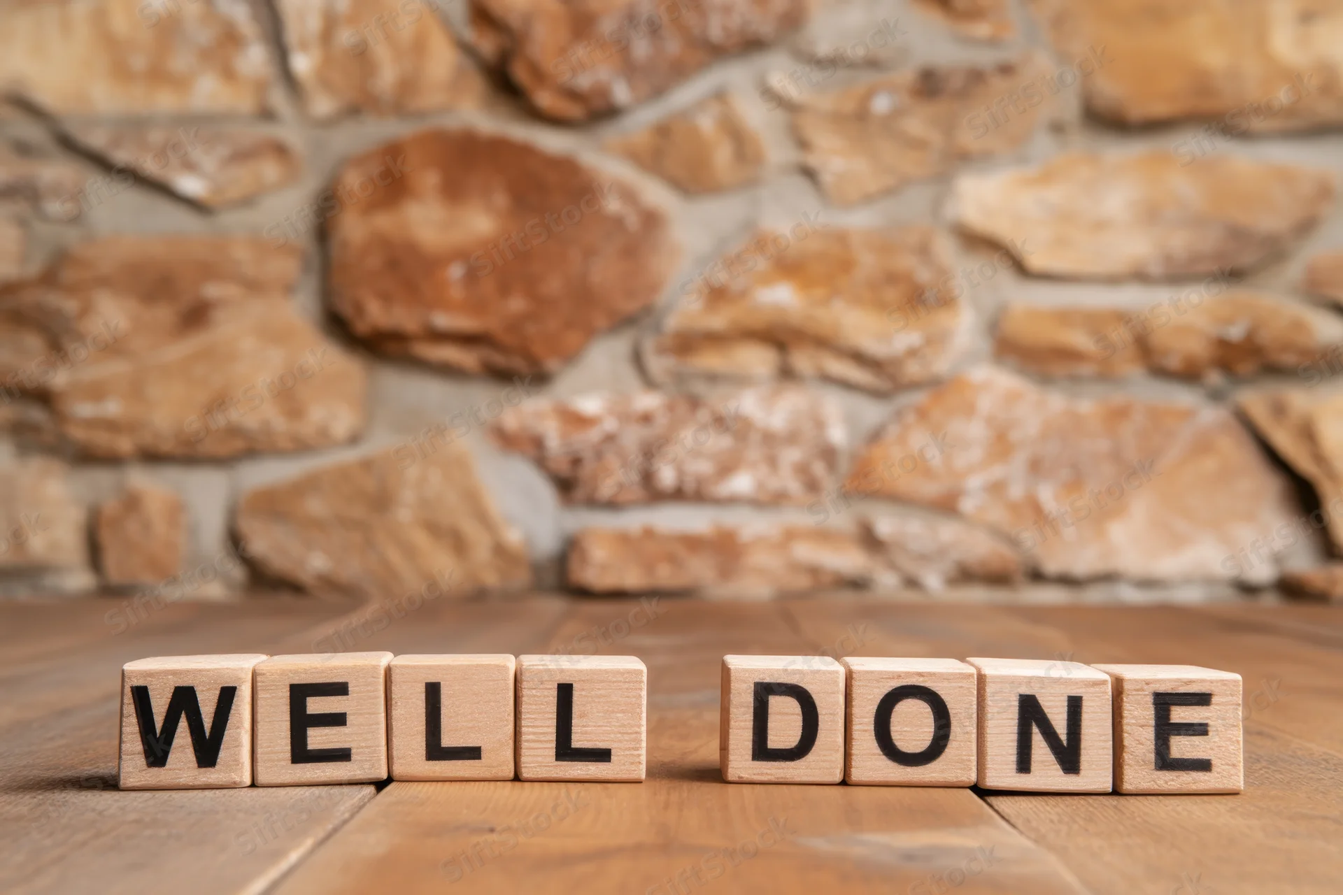 Wooden blocks spelling well done arranged on a wooden table in front of a stone wall