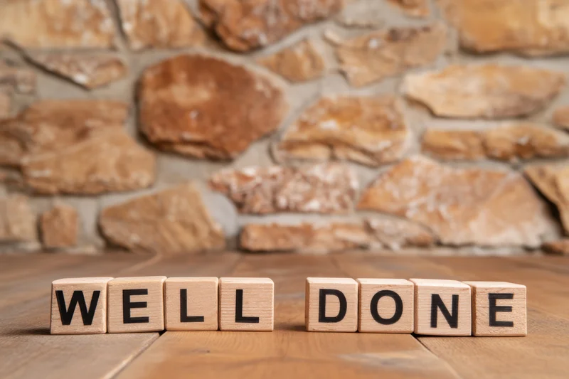 Wooden blocks spelling well done arranged on a wooden table in front of a stone wall