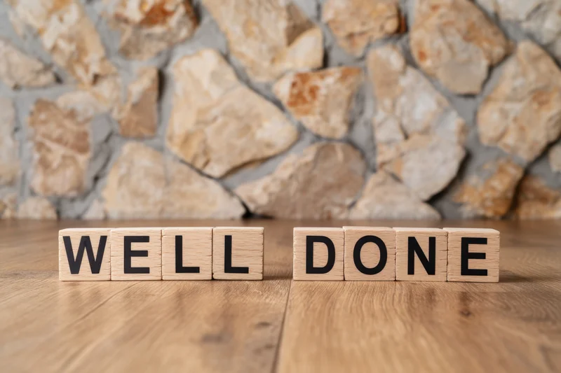 Wooden blocks spelling well done arranged on a wooden table in front of a stone wall