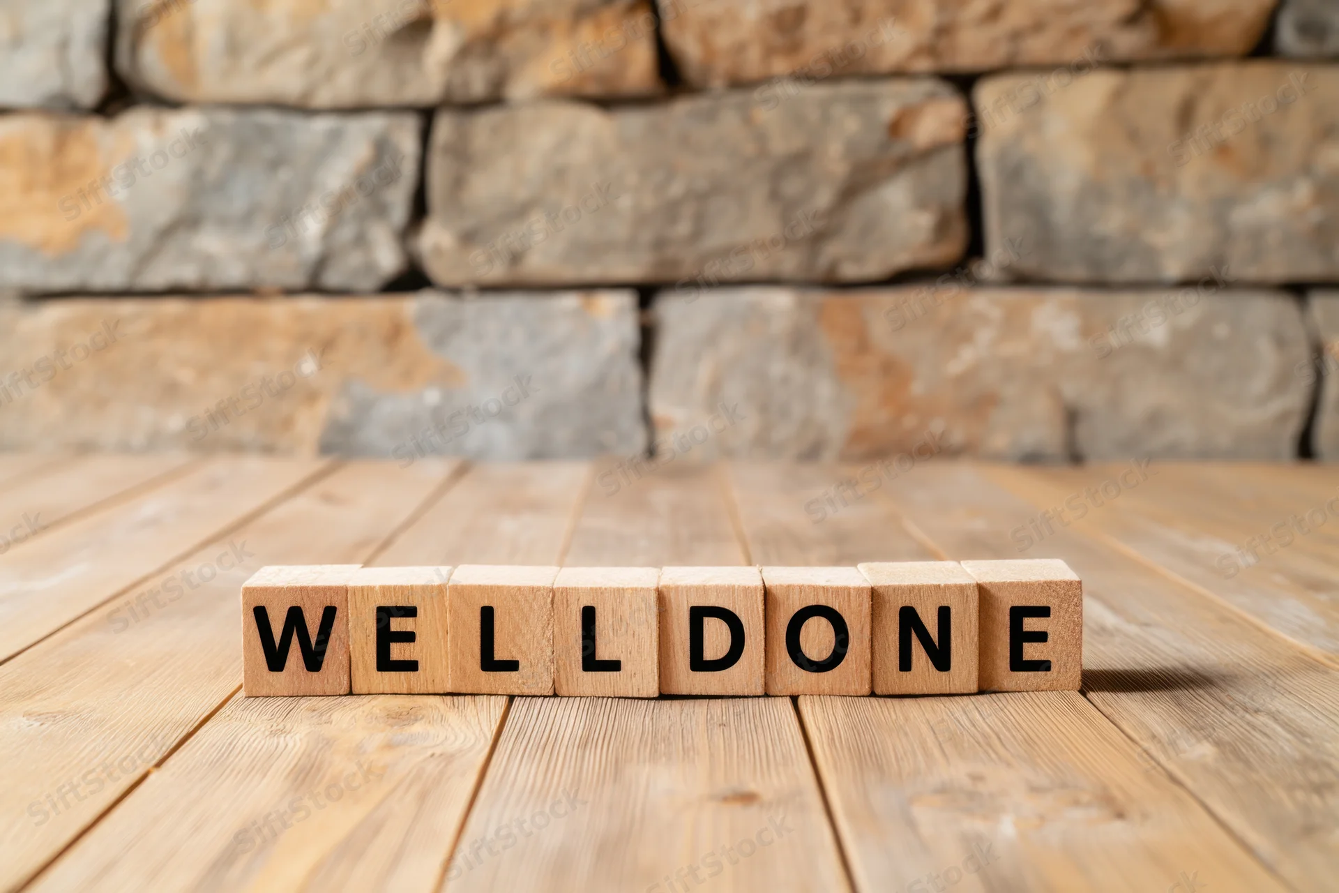 Wooden blocks spelling well done arranged on a wooden floor in front of a stone wall