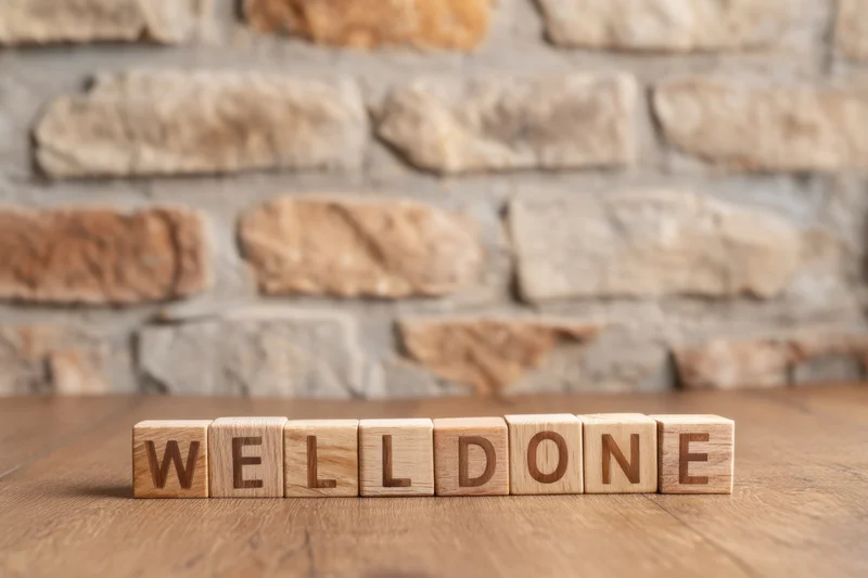 Wooden blocks spelling well done arranged on a rustic wooden table with stone wall background