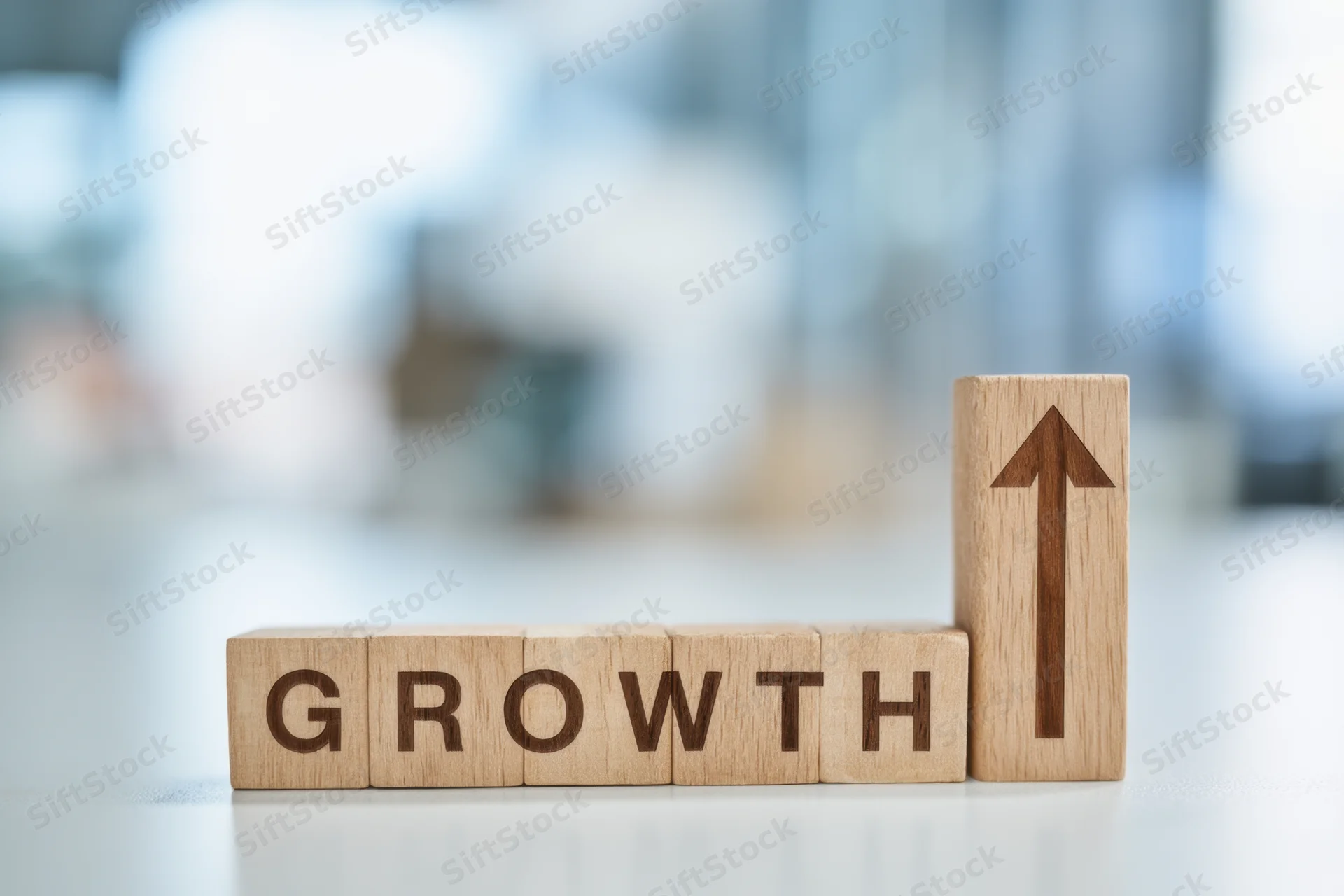 Wooden blocks spelling growth with upward arrow on desk in office setting