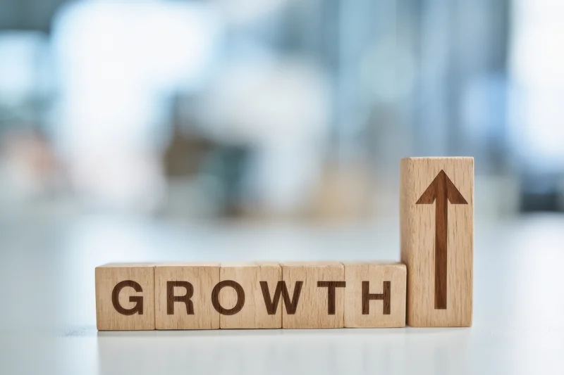 Wooden blocks spelling growth with upward arrow on desk in office setting