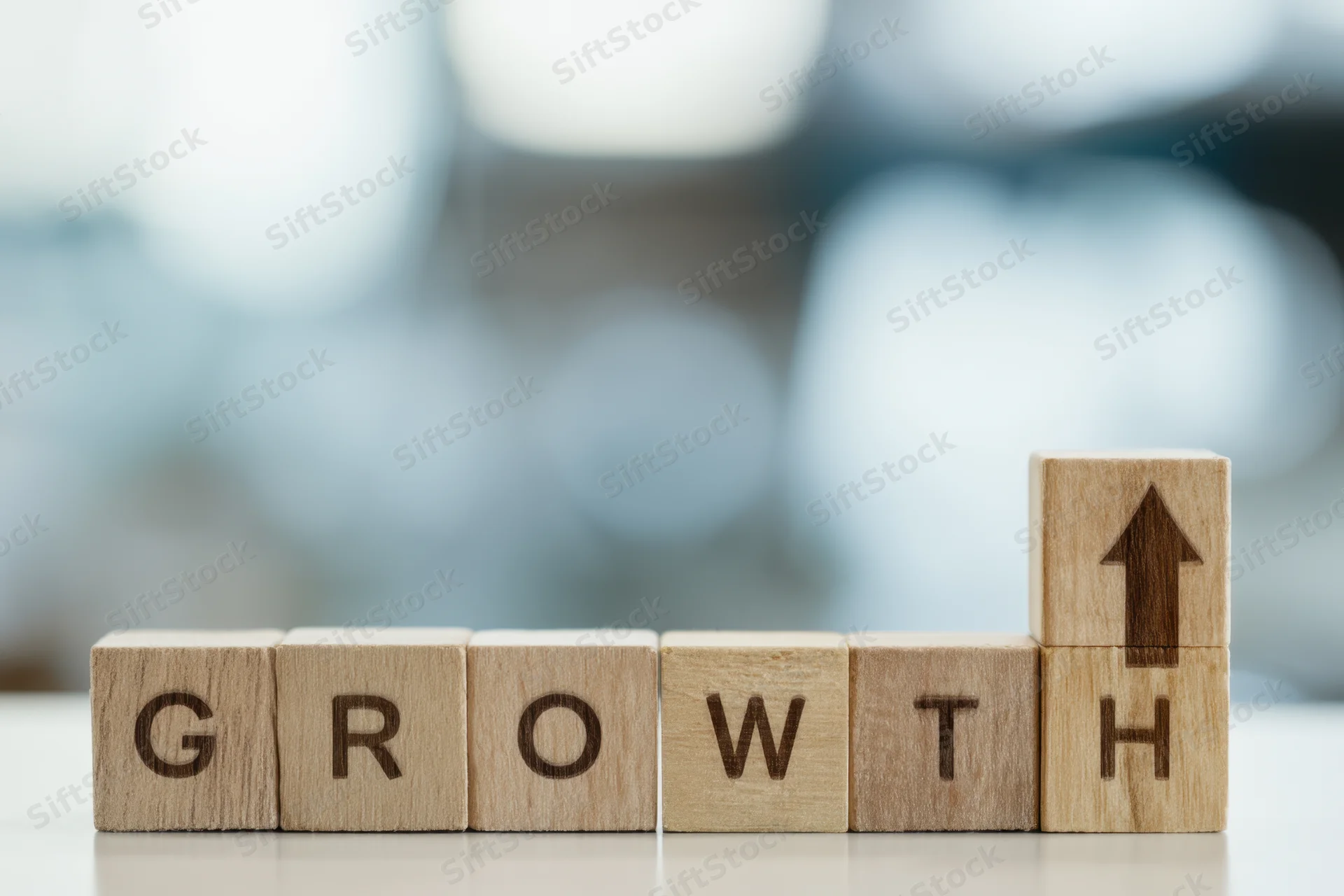 Wooden blocks spelling growth with an upward arrow on the last block on a desk with blurred background