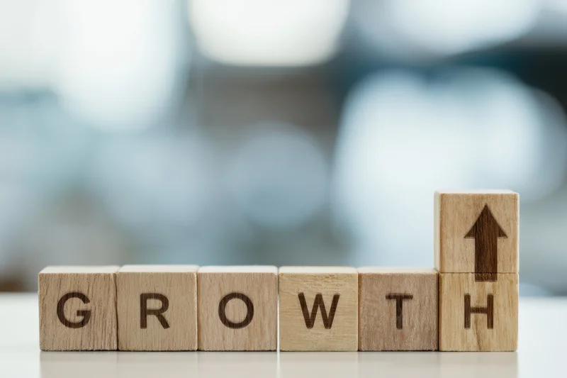 Wooden blocks spelling growth with an upward arrow on the last block on a desk with blurred background