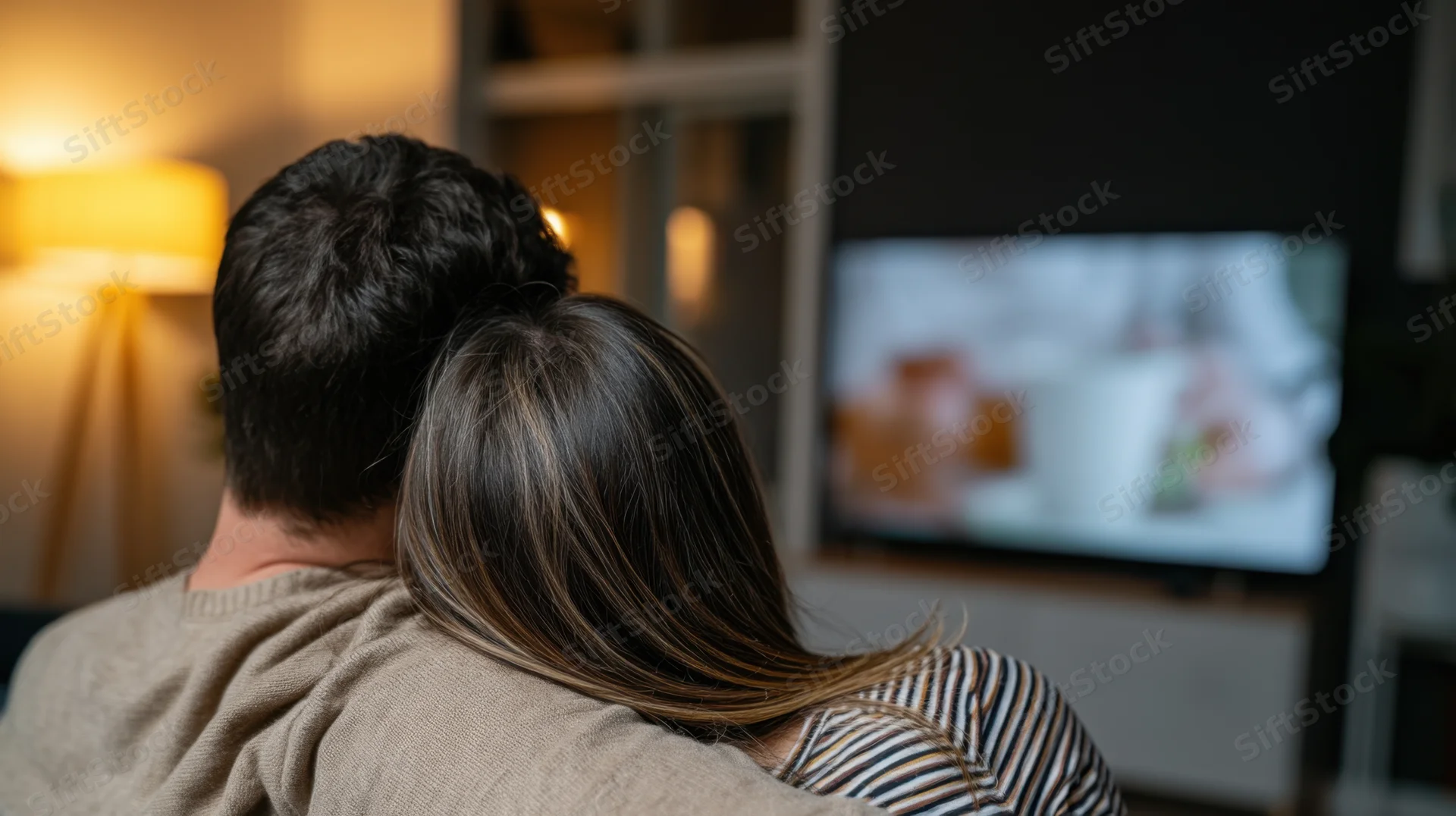 Couple sitting on couch watching television in living room at evening