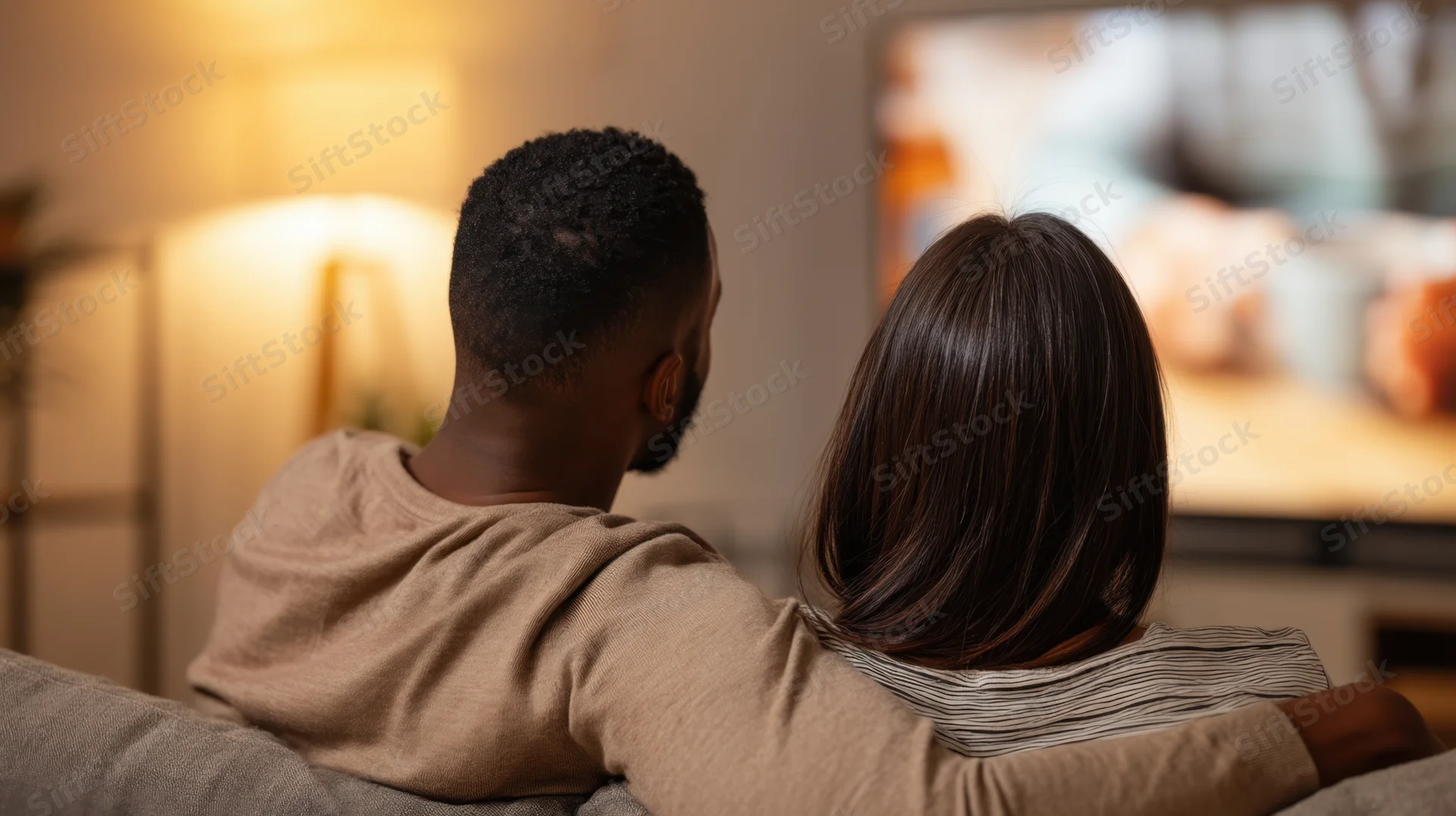 Couple sitting on couch watching television in living room at evening