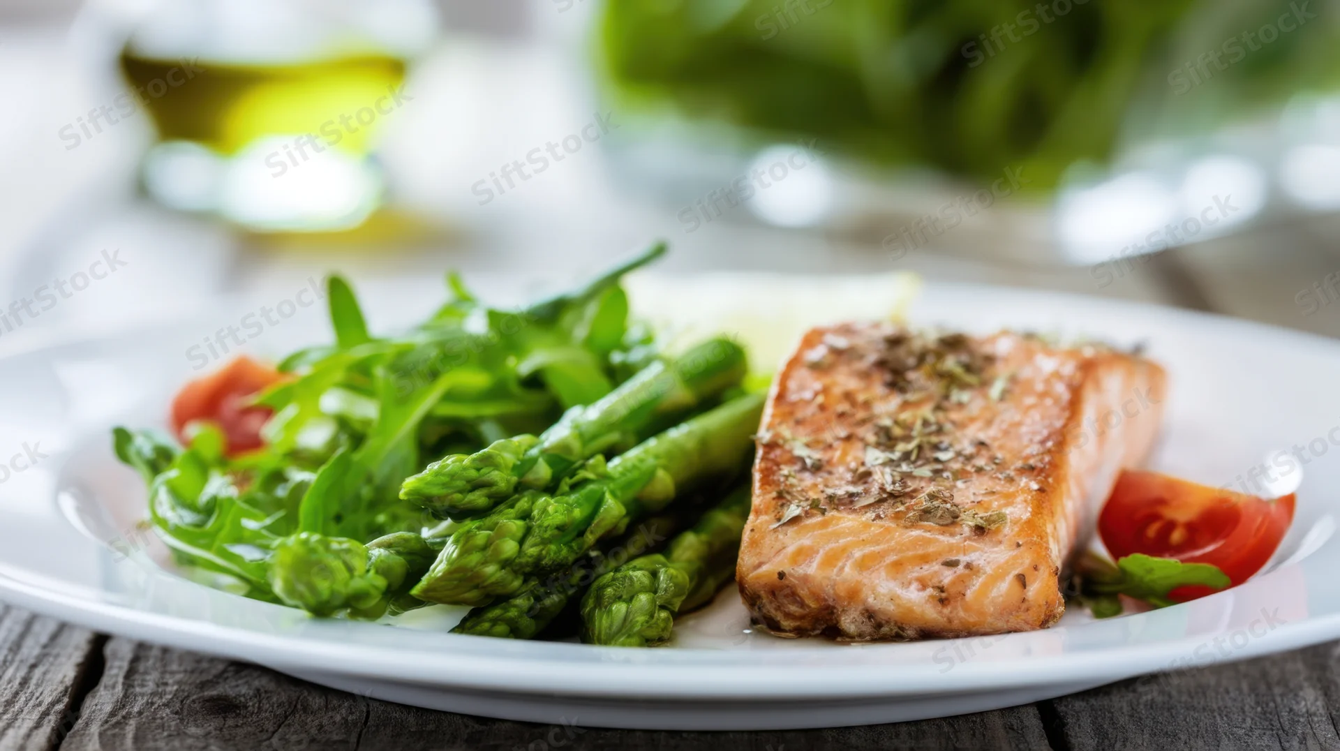 Roasted salmon fillet with asparagus and salad on a white plate on wooden table