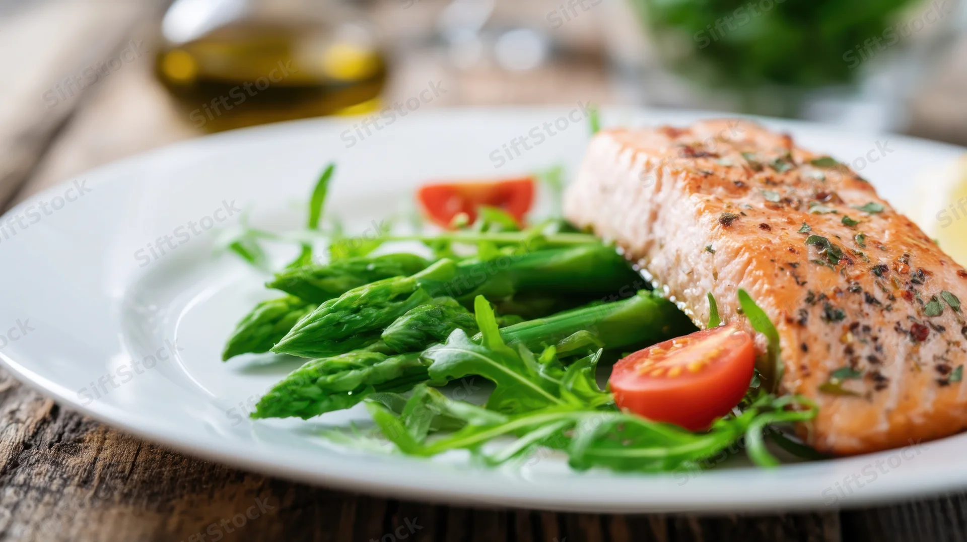 Roasted salmon fillet served with asparagus and arugula salad on a white plate on a wooden table
