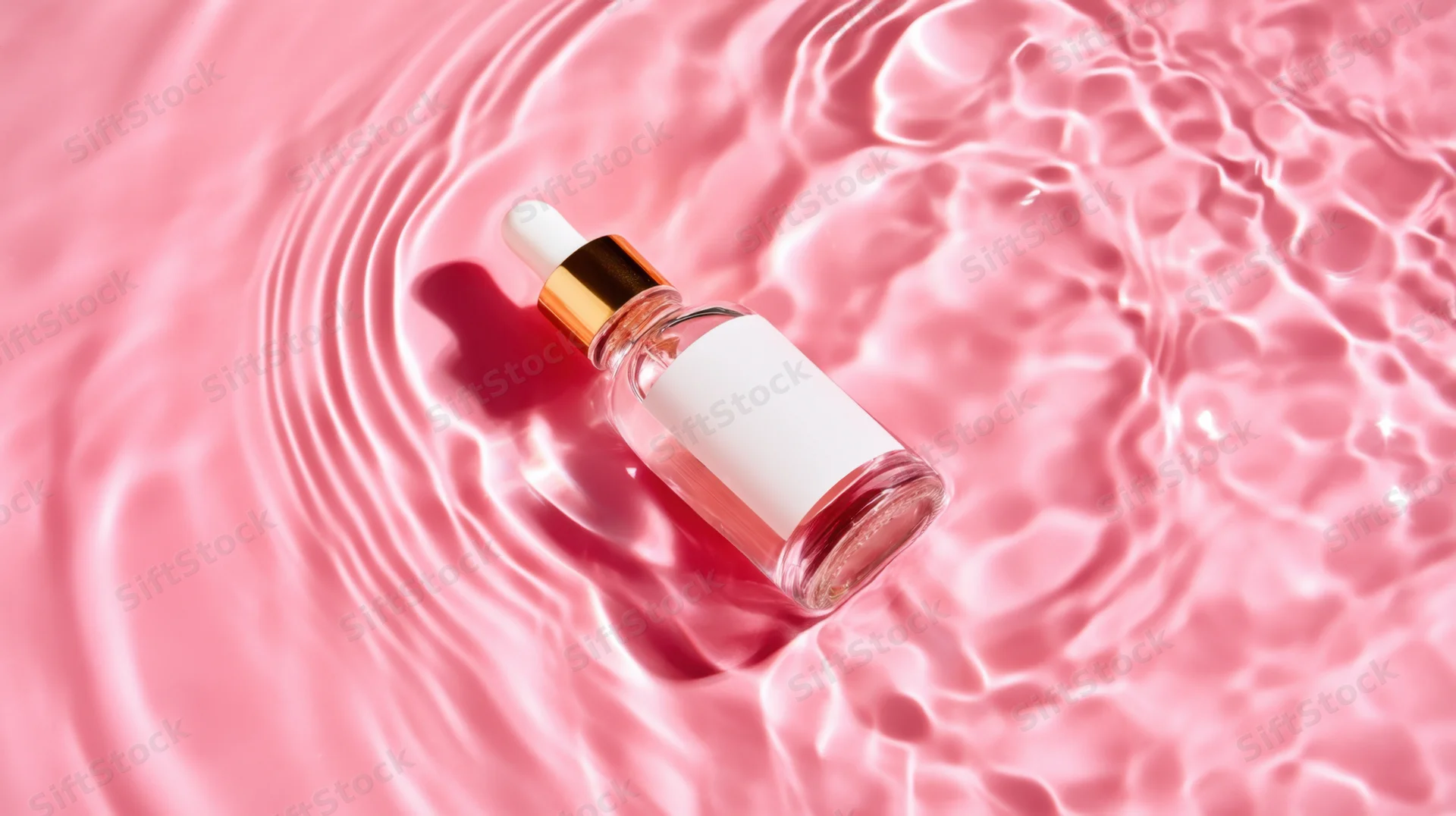 Clear glass dropper bottle with gold cap floating in pink water with ripples and reflections