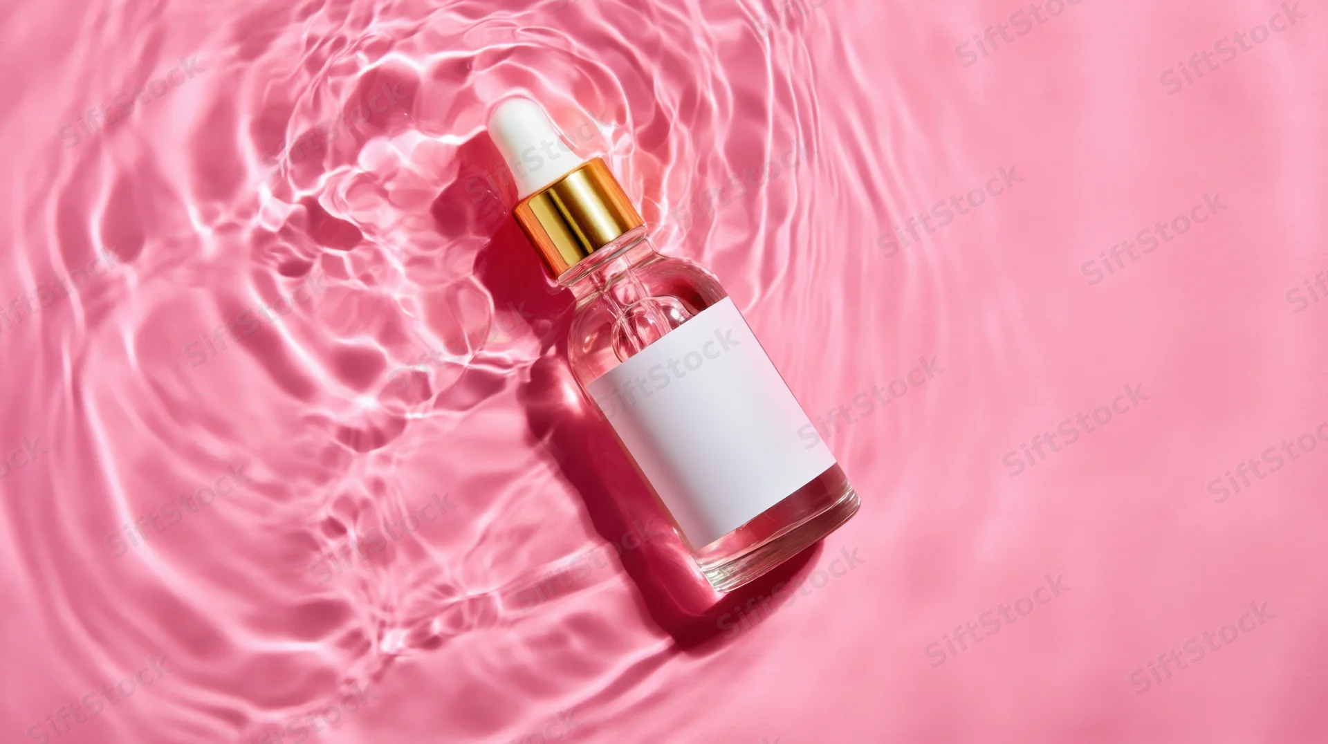 Clear glass dropper bottle with gold cap and white label floating in rippling pink water
